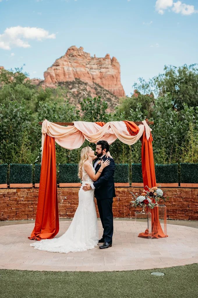 Sedona wedding ceremony arch with terracotta and blush draping beneath Bell Rock