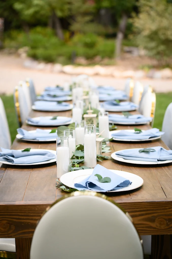 Long farm table reception with dusty blue napkins, eucalyptus runner and pillar candles