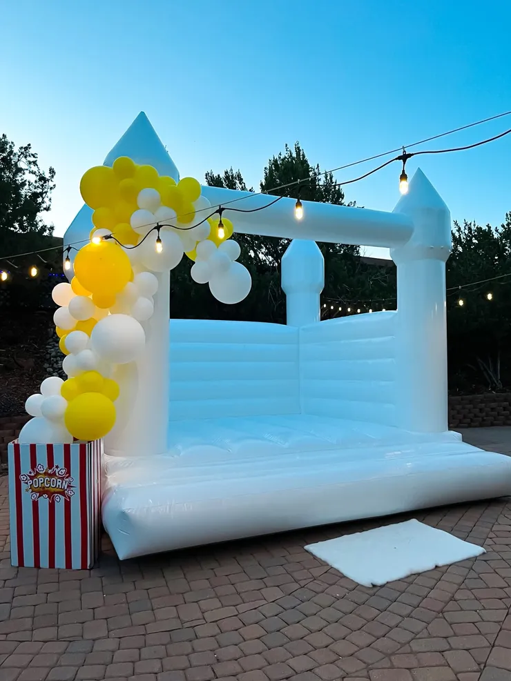 White bounce house at dusk with yellow balloon arch and popcorn cart