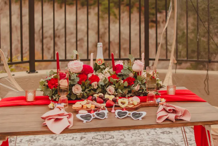 Galentine's sweetheart table with red roses, champagne and heart sunglasses