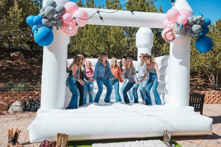 Friends jumping in a white bounce house with balloon garland
